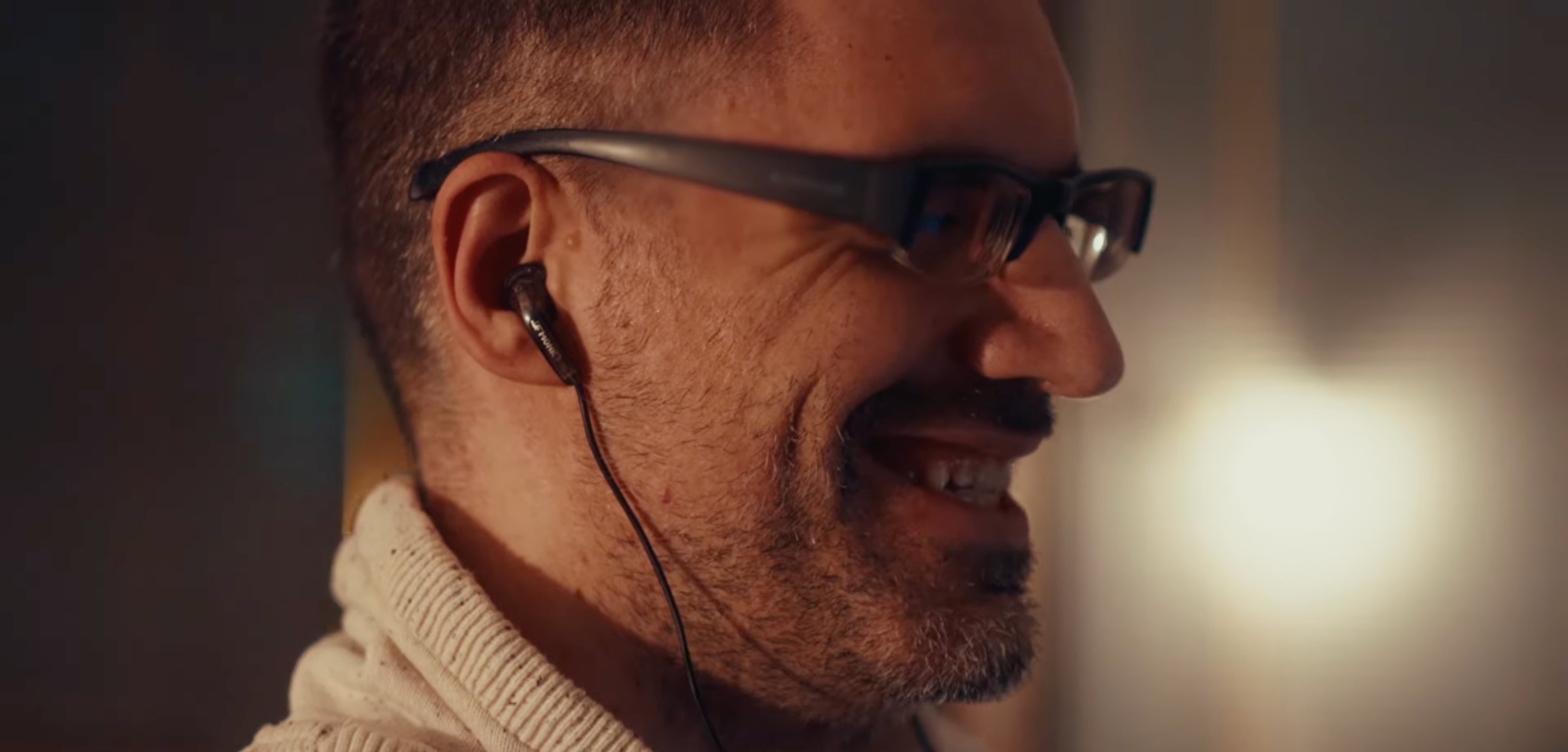 ALT TEXT: Ertay Shashko wears earphones and smiles while he is at his desk working remotely.